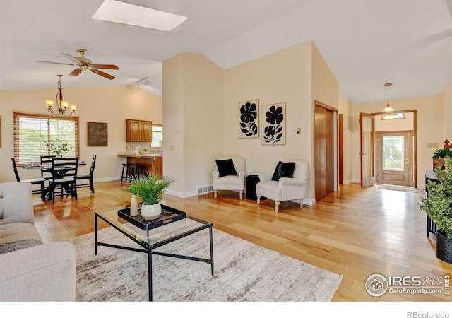living room with vaulted ceiling, a skylight, light wood finished floors, a chandelier, and ceiling fan