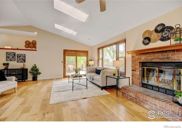 living area with a brick fireplace, wood finished floors, ceiling fan, high vaulted ceiling, and a skylight