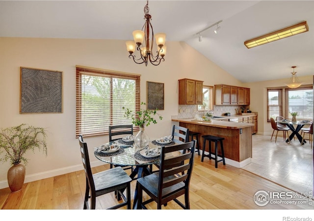 dining area featuring lofted ceiling, rail lighting, a chandelier, light wood-style floors, and baseboards