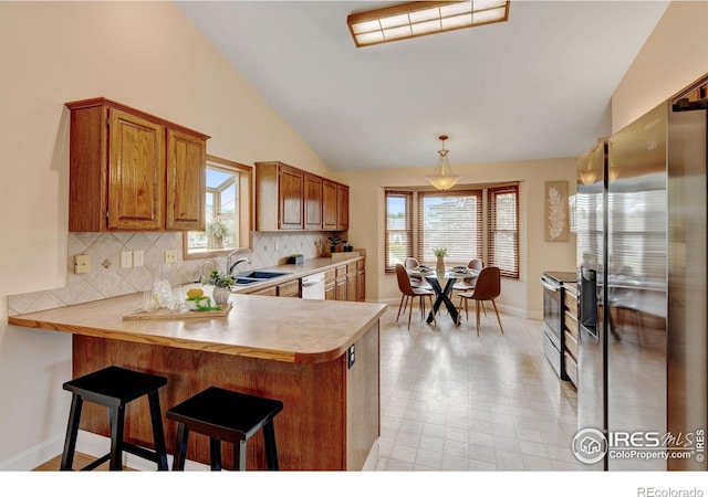 kitchen featuring appliances with stainless steel finishes, vaulted ceiling, a sink, light countertops, and a peninsula