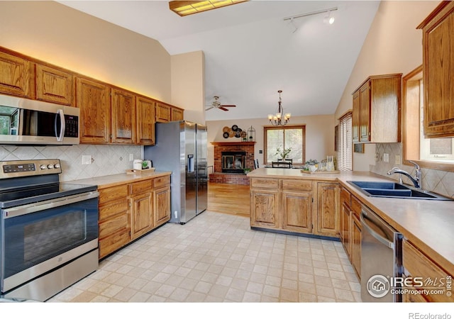 kitchen with stainless steel appliances, a sink, track lighting, a brick fireplace, and light countertops