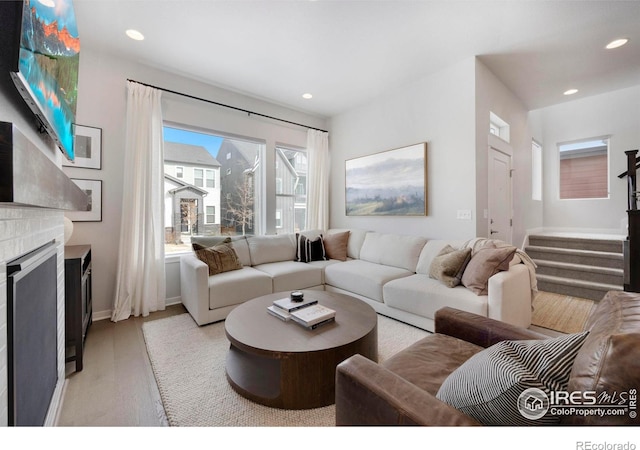 living area featuring light wood finished floors, stairs, recessed lighting, a large fireplace, and baseboards
