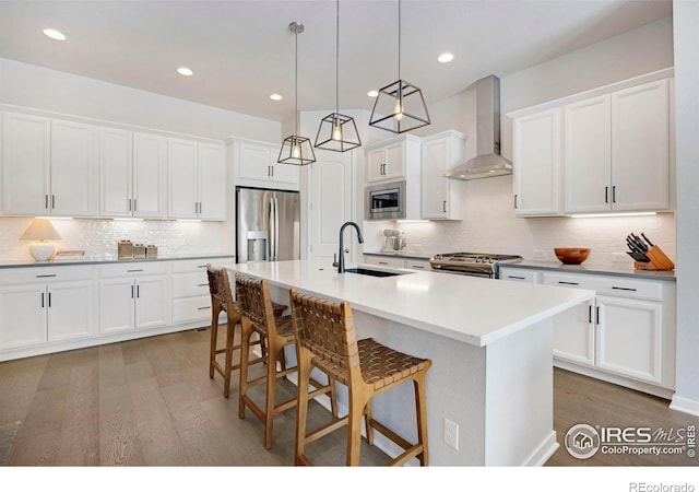 kitchen featuring stainless steel appliances, wall chimney range hood, a sink, wood finished floors, and backsplash