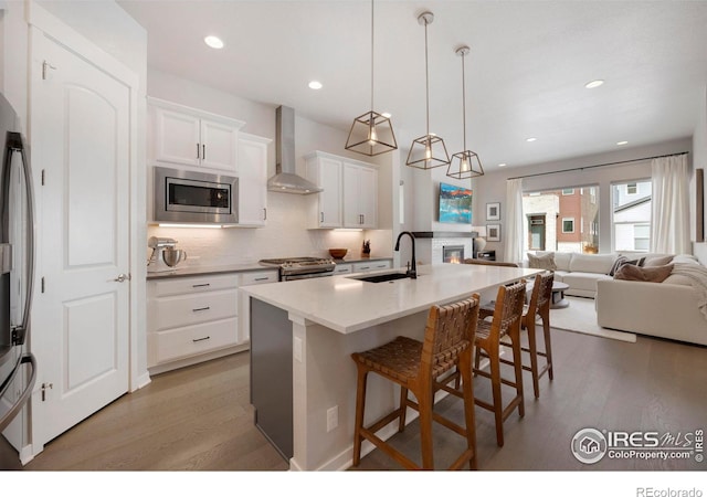 kitchen featuring appliances with stainless steel finishes, a sink, wall chimney range hood, light wood finished floors, and recessed lighting