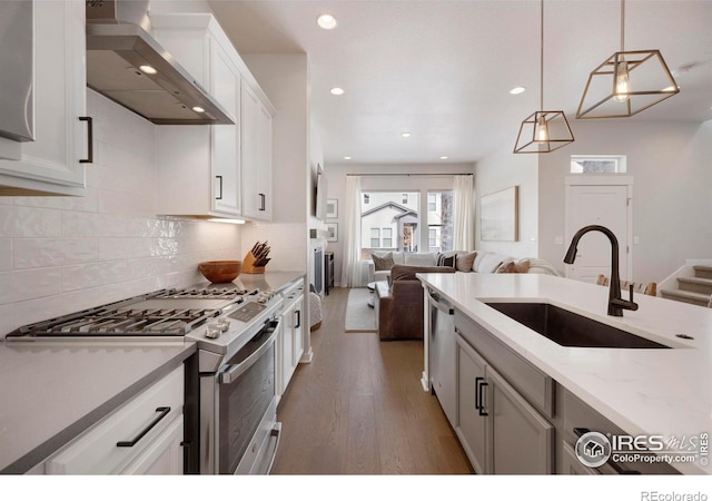 kitchen with appliances with stainless steel finishes, wall chimney exhaust hood, a sink, open floor plan, and wood finished floors