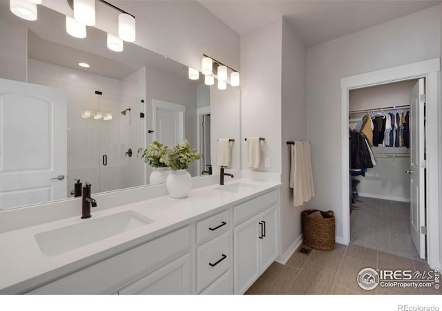 bathroom with a shower stall, double vanity, a spacious closet, baseboards, and tile patterned flooring