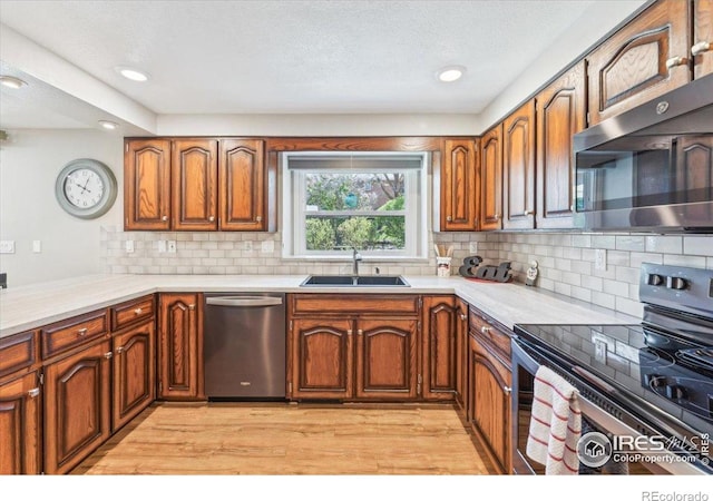 4880 Filbert Dr, Loveland, CO 80538 - kitchen with stainless steel appliances, a sink, brown cabinetry, light wood finished floors, and a textured ceiling
