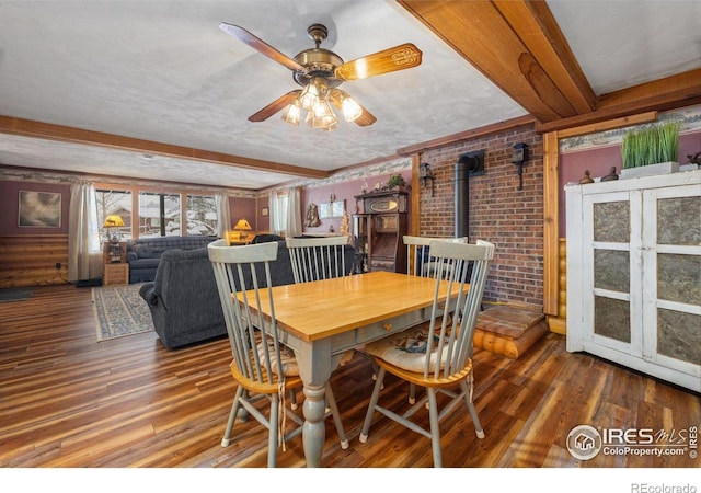 1810 N Ridge Ln, Estes Park, CO 80517 - dining space featuring a wood stove, wood finished floors, a ceiling fan, beamed ceiling, and brick wall