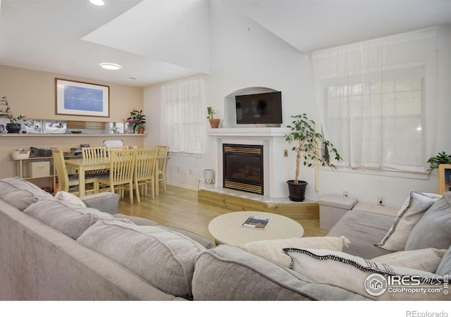 living area with wood finished floors, a glass covered fireplace, recessed lighting, baseboards, and lofted ceiling