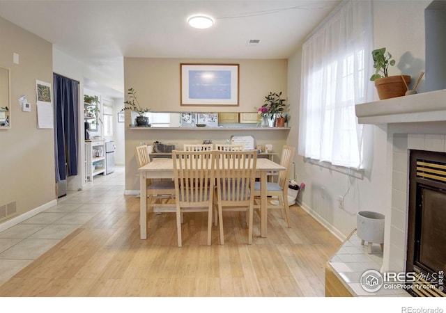 dining space featuring light wood-style floors, healthy amount of natural light, and a tiled fireplace