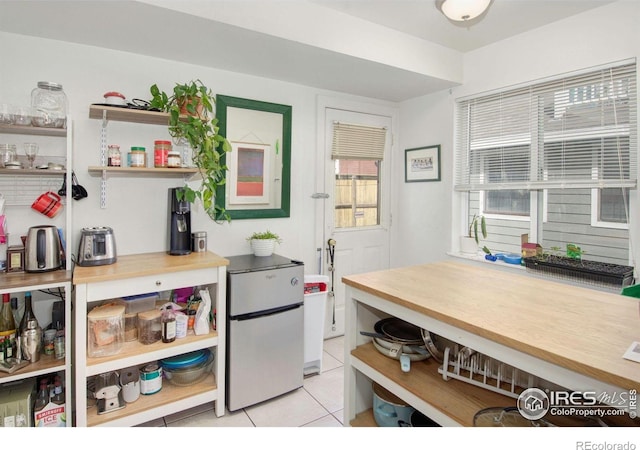 kitchen with open shelves, freestanding refrigerator, light tile patterned floors, and butcher block countertops
