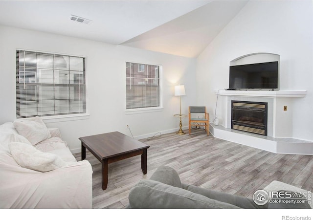 living room with wood finished floors, baseboards, a glass covered fireplace, and vaulted ceiling