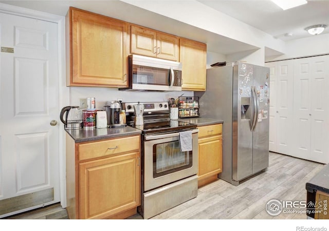 kitchen featuring appliances with stainless steel finishes, light wood-style floors, dark countertops, and light brown cabinetry
