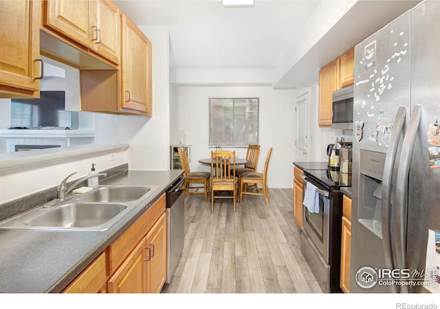 kitchen featuring appliances with stainless steel finishes, a sink, light wood-style floors, and dark countertops