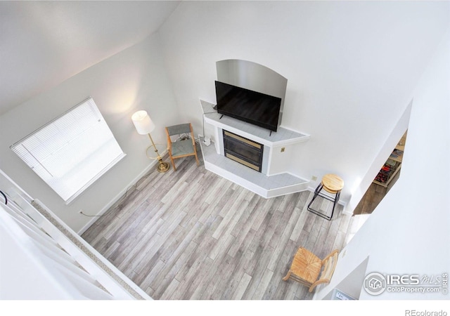 living area with a glass covered fireplace, wood finished floors, baseboards, and vaulted ceiling