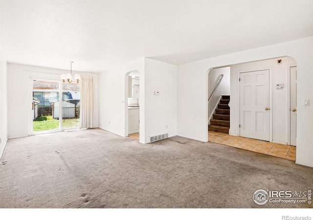 unfurnished living room featuring carpet floors, arched walkways, stairway, a chandelier, and tile patterned floors