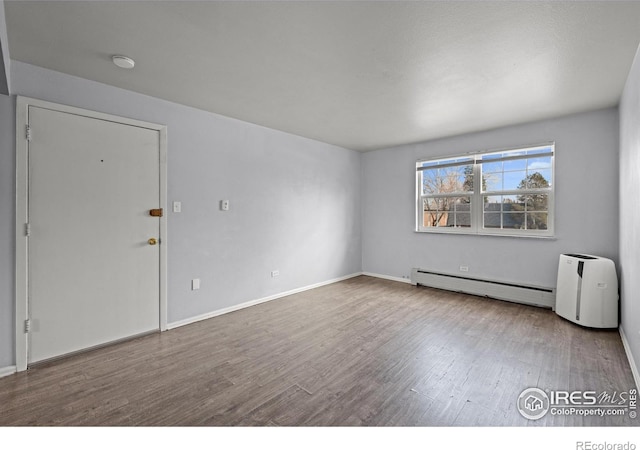 unfurnished room featuring baseboard heating, wood finished floors, baseboards, and a smoke detector
