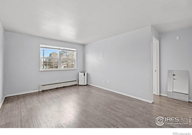 empty room featuring baseboard heating, wood finished floors, and baseboards