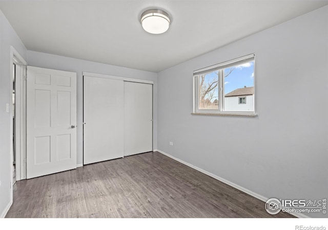 unfurnished bedroom with wood finished floors, baseboards, and a closet
