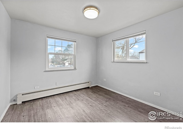 spare room featuring a baseboard radiator, healthy amount of natural light, wood finished floors, and baseboards