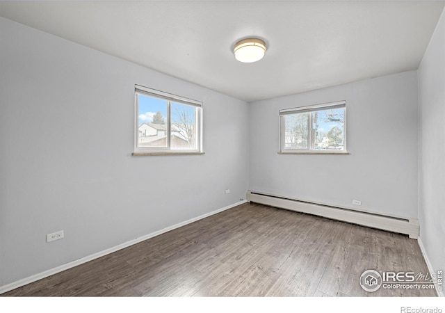 spare room with a baseboard heating unit, wood finished floors, and baseboards