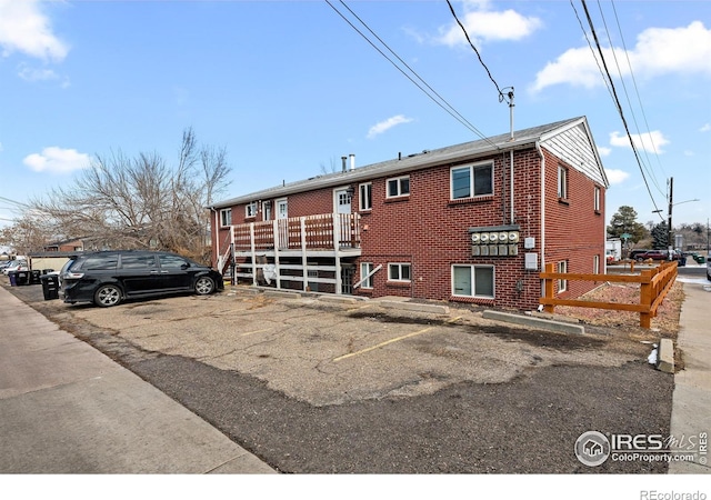 rear view of property featuring uncovered parking, brick siding, and a deck