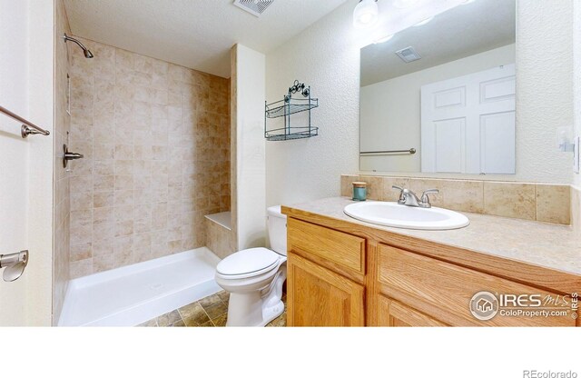 bathroom featuring a tile shower, toilet, and vanity