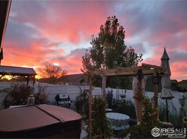patio terrace at dusk featuring a fenced backyard, a pergola, a hot tub, and a grill