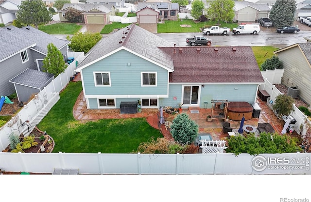 rear view of property featuring a residential view, a fenced backyard, a hot tub, central AC, and a shingled roof