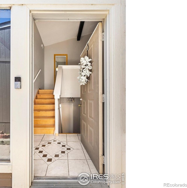 corridor with vaulted ceiling, tile patterned flooring, and stairway
