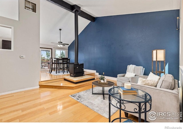 living area featuring wood finished floors, a wood stove, baseboards, and ceiling fan