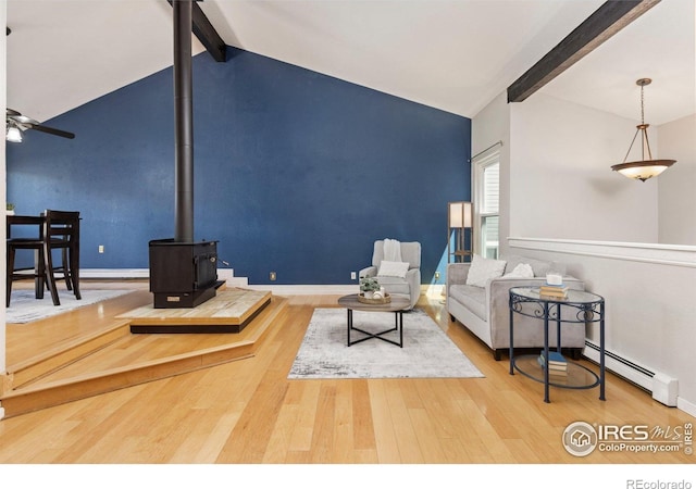living area featuring baseboard heating, a wood stove, wood finished floors, a ceiling fan, and baseboards
