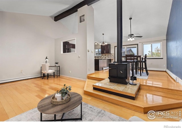 living area with a wood stove, wood finished floors, a ceiling fan, and baseboards