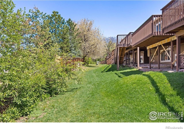 view of grassy yard with stairs and a deck