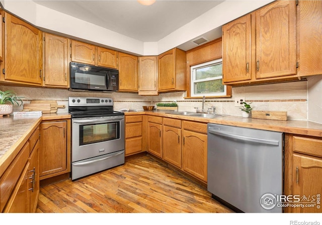 kitchen featuring appliances with stainless steel finishes, a sink, tasteful backsplash, light wood-type flooring, and light countertops