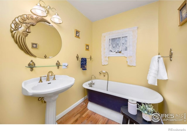 bathroom featuring baseboards, wood finished floors, and a soaking tub