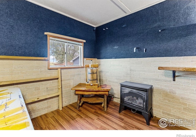 misc room featuring a wood stove, tile walls, ornamental molding, wood finished floors, and a wainscoted wall