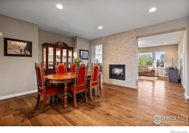 dining room with light wood-style floors, a multi sided fireplace, recessed lighting, and baseboards