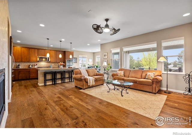 living room with wood-type flooring, a ceiling fan, recessed lighting, a fireplace, and baseboards