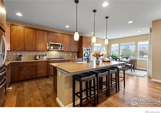 kitchen with appliances with stainless steel finishes, dark wood-type flooring, decorative backsplash, light countertops, and recessed lighting