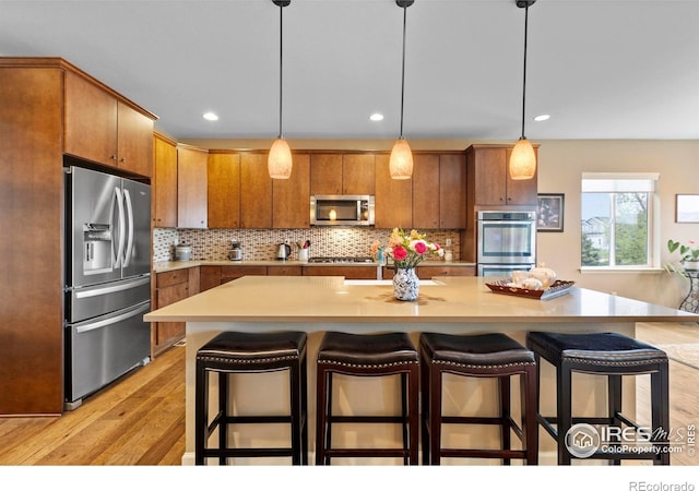 kitchen featuring appliances with stainless steel finishes, brown cabinetry, light wood-type flooring, decorative backsplash, and light countertops