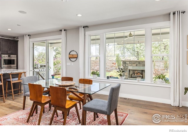dining room with a stone fireplace, recessed lighting, light wood-style flooring, and baseboards