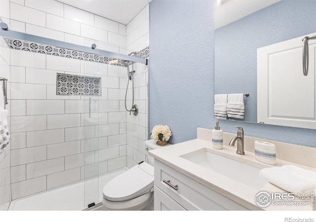 bathroom with a textured wall, a tile shower, toilet, and vanity