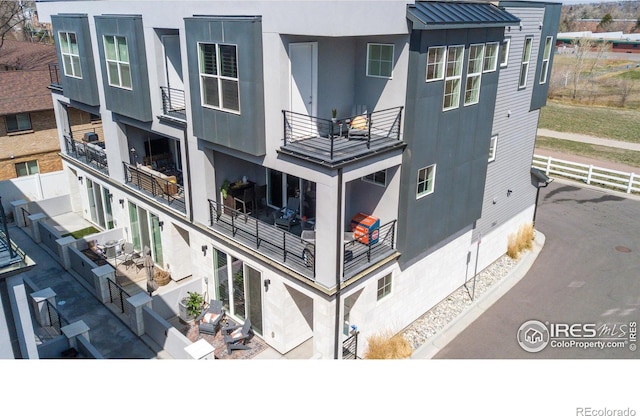 back of house featuring a balcony, stucco siding, and fence
