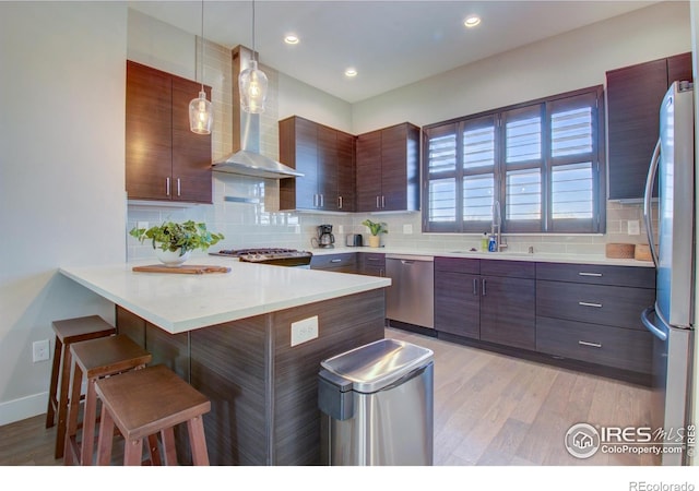 7861 W 51st Ave, Arvada, CO 80002 - kitchen with appliances with stainless steel finishes, wall chimney exhaust hood, a breakfast bar area, light wood-style flooring, and recessed lighting