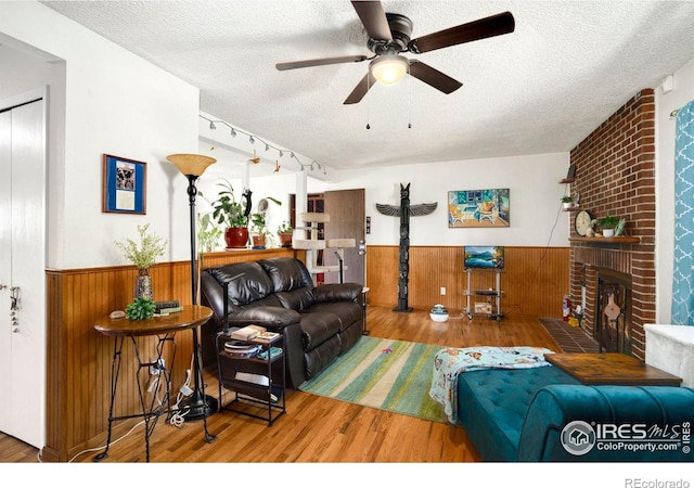 living area featuring a textured ceiling, wood finished floors, a wainscoted wall, wooden walls, and a ceiling fan