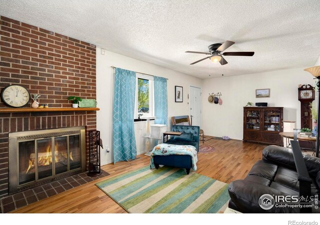 living room featuring wood finished floors, a ceiling fan, a fireplace, and a textured ceiling