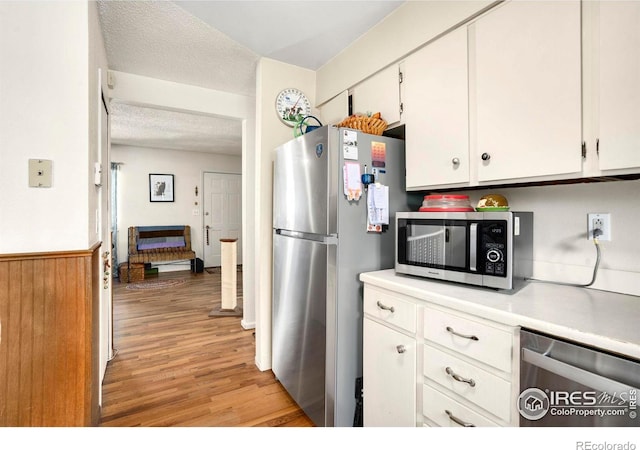 kitchen with stainless steel appliances, light wood-type flooring, white cabinets, light countertops, and a textured ceiling