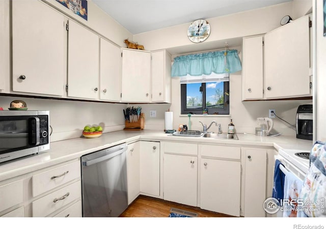 kitchen with appliances with stainless steel finishes, a sink, light countertops, and white cabinetry