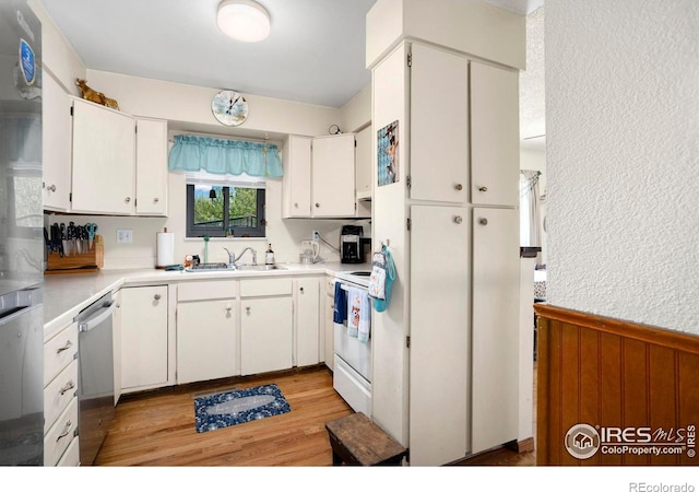 kitchen featuring stainless steel appliances, wainscoting, light countertops, white cabinetry, and light wood-style floors